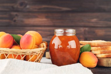 Kayısı, kavanoz ve ekmek tostu, kahverengi ahşap arka planda peçete.