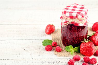 Cam kavanozda tatlı ahududu reçeli ve beyaz ahşap masada olgun böğürtlen.