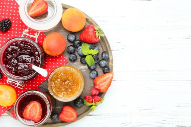 Cam kavanozlarda tatlı reçel, olgun böğürtlenler beyaz ahşap masada.