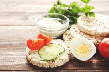 Krem peynirli çıtır ekmek, kahverengi ahşap masada yumurta ve sebze.