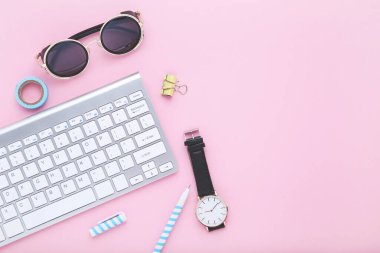 Pembe arka planda güneş gözlüğü ve kol saati olan bilgisayar klavyesi