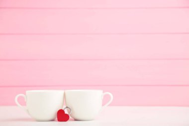 Beyaz bardaklar ve pembe arka planda kalp şeklinde kırmızı asma kilit.