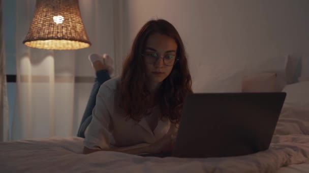 Młoda skoncentrowana kobieta pracująca w nocy w sypialni za pomocą laptopa i wpisując wiadomość — Wideo stockowe