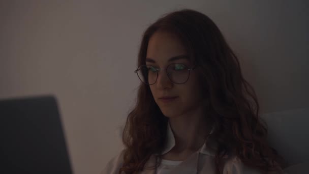 Primer plano de la joven mujer concentrada que trabaja por la noche en su dormitorio con el ordenador portátil — Vídeos de Stock