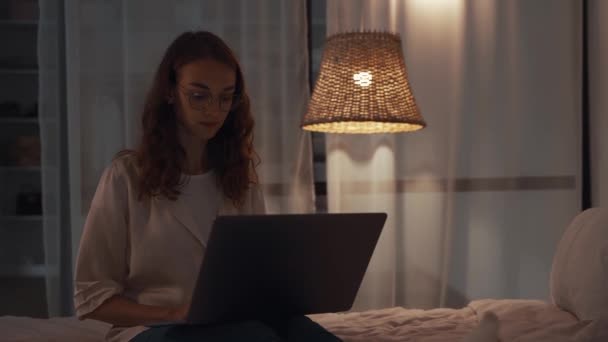 Young concentrated woman working at night in her bedroom using laptop computer and typing message — Stock Video
