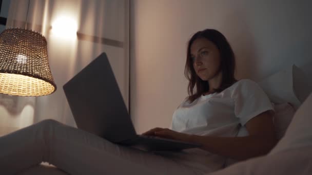 ベッドの上に横たわっラップトップコンピュータを使用して彼女の寝室で夜に働く女性 — ストック動画