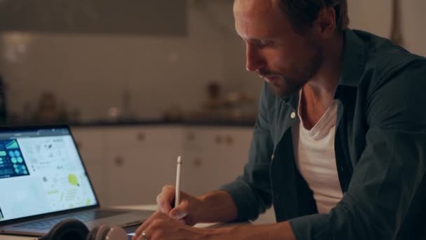 Człowiek pracujący w nocy w kuchni za pomocą tabletu i słuchać muzyki ze słuchawkami — Wideo stockowe