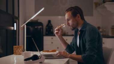 Geceleri evde çalışan, pizza yiyen ve dizüstü bilgisayarda yazan bir adam.