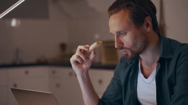 Hombre trabajando de noche en casa, comiendo pizza y escribiendo en el portátil — Vídeos de Stock