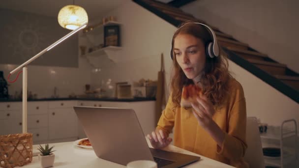 Las mujeres trabajan por la noche, comiendo pizza, escribiendo en el portátil y escuchando música — Vídeos de Stock