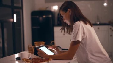 Geceleri tabletle çalışan bir kadın. Bayan öğrenci akşam mutfağında internetten öğreniyor.