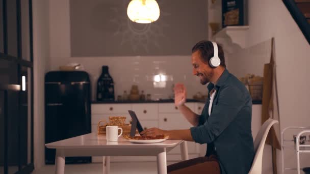 Männlicher Freiberufler führt Videoanrufe mit einem Kunden, schaut auf einen Tablet-Bildschirm und diskutiert ein neues Startup-Projekt, während er von seinem Home Office aus arbeitet. — Stockvideo