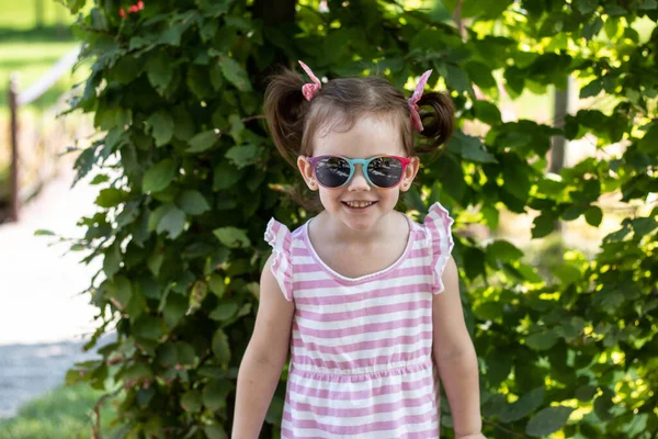 Kleines Mädchen Gestreiftem Kleid Und Sonnenbrille Blickt Lächelnd Die Kamera — Stockfoto