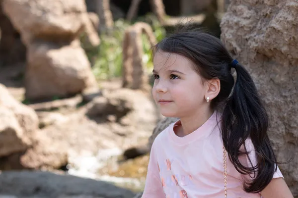 一个快乐的小女孩 一头乌黑的长发 背景是一个石子花园 — 图库照片
