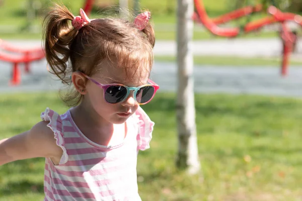 Kleines Fröhliches Mädchen Mit Pferdeschwanz Und Sonnenbrille Auf Einem Sommerspielplatz — Stockfoto