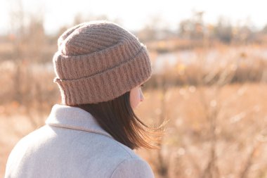 Örgü şapkalı yüzü olmayan bir kız, bir arka plan ve soluk bir nehir manzarasının arka planında duran bir cekete karşı duruyor.