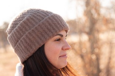 Örgü şapkalı ve ceketli gülümseyen kız sonbahar çöl manzarasının arka planında duruyor.