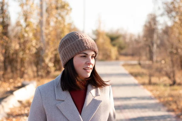 Örgü şapkalı ve ceketli gülümseyen kız terk edilmiş bir park gölünün kaldırımlı yolunda yürüyor.