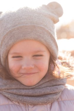 Smiling little child in a warm hat with ears smiling in the sunlight on a walk