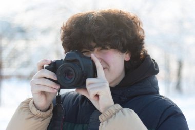 Siyah kıvırcık saçlı bir çocuk DSLR kamerasıyla fotoğraf çekiyor. Açık havada harika bir kış fotoğrafı.