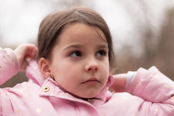 Sarı saçlı, atkuyruklu, ceketli güzel bir kız sonbahar arka planında dikiliyor. Üzülerek yukarı bakıyor.