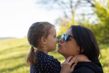 Anne ve küçük kızı gün batımında çayırda eğleniyorlar.