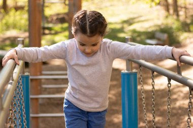 Schoolgirl in a gray turtleneck sweater and blue jeans plays on the playground