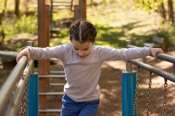 Schoolgirl in a gray turtleneck sweater and blue jeans plays on the playground
