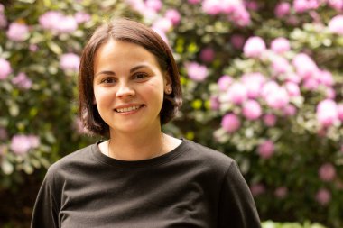 Bir yaz parkında siyah tişörtlü tatlı bir kız çiçek açan bir rhododendronun arka planına karşı.