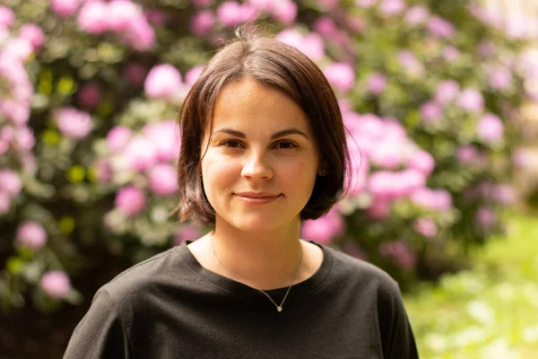 Çiçekli bir çalılığın arkasında siyah tişörtlü güzel bir kadının portresi.