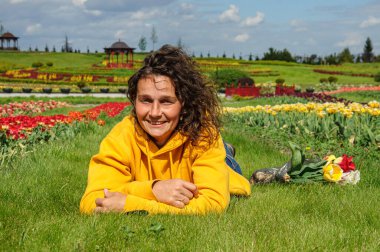 Parlak kazaklı genç bir kadın lalelerin arasındaki yeşil çimenlerde yatıyor.