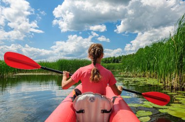 A sporty woman in bright clothes is rowing a red kayak along the Zdvizh River. Ukraine