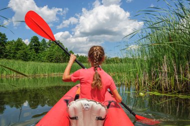 A sporty woman in bright clothes is rowing a red kayak along the Zdvizh River. Ukraine
