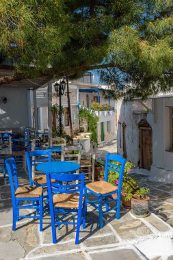 Yunanistan 'ın başkenti Paros Adası' nda beyazlatılmış evleri ve mavi demir masaları ve tahta sandalyeleri olan geleneksel bir kafenin dış cephesi olan sikladitik bir sokak.