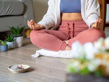 Kadın evde kristaller ve bitkilerle meditasyon yapıyor. Sessiz ve rahatlatıcı bir odada meditasyon yapan genç bir adam bir yastığın üzerinde lotus pozisyonunda oturuyor. Ruh sağlığı ve stres atımı.