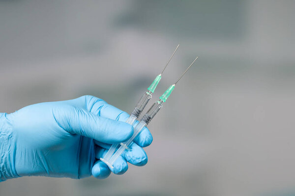 Close up of doctor's hand in medical gloves with two syringes of coronavirus or flu vaccine