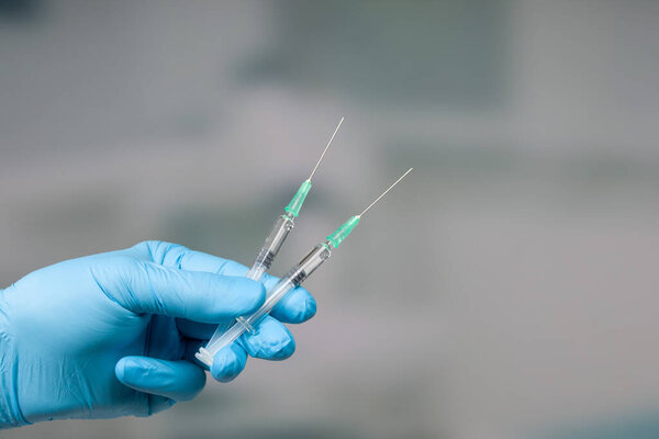 Close up of doctor's hand in medical gloves with two syringes ready for injection 