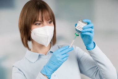 female doctor or nurse with syringe is pulling up coronavirus vaccine wearing a ffp2 mask and medical gloves for protection