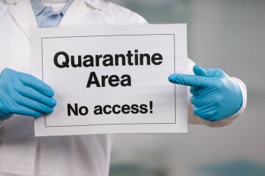 Doktorun elinde tıbbi eldivenler var. Polis merkezinin önünde karantina işareti var.