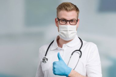 Steteskoplu erkek doktor tıbbi maske ve tıbbi eldivenlerle korunuyor.