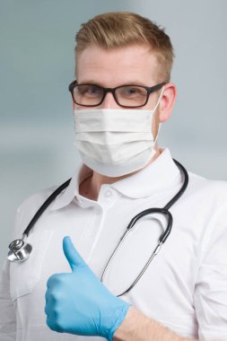 Steteskoplu erkek doktor tıbbi maske ve tıbbi eldivenlerle korunuyor.