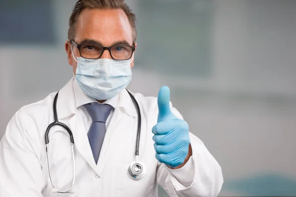 医療用フェイスマスクと医療用手袋を着用した男性医師が親指を立てています — ストック写真