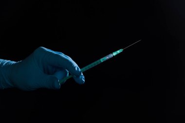 Doktorun elini siyah arka planda aşı şırıngası ile tıbbi eldivenlerle kapat.