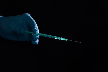 Doktorun elini siyah arka planda aşı şırıngası ile tıbbi eldivenlerle kapat.