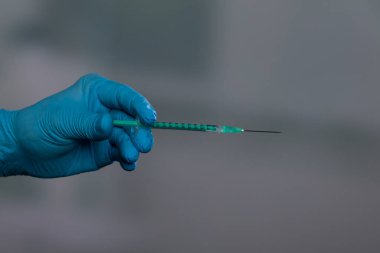 Doktorun elini tıbbi eldivenlerle klinik arka planında aşı şırıngası ile kapat.