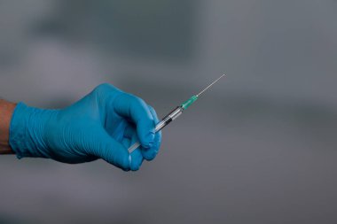 Doktorun elini tıbbi eldivenlerle klinik arka planında aşı şırıngası ile kapat.