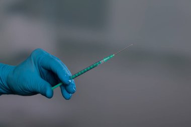 Doktorun elini tıbbi eldivenlerle klinik arka planında aşı şırıngası ile kapat.