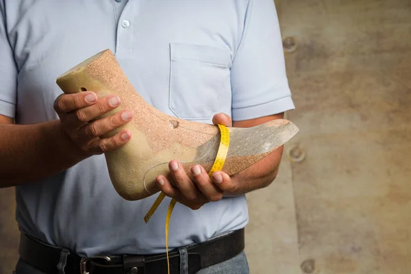 Close-up of hands of an orthopedic shoemaker presenting an individual made wooden last