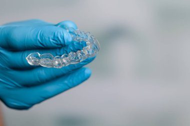 Diş hekimi mavi eldivenlerle dişçi odasının önünde şeffaf, çıkarılabilir bir sıralayıcı sunuyor.