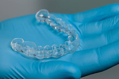 Diş hekimi mavi eldivenlerle dişçi odasının önünde şeffaf, çıkarılabilir bir sıralayıcı sunuyor.